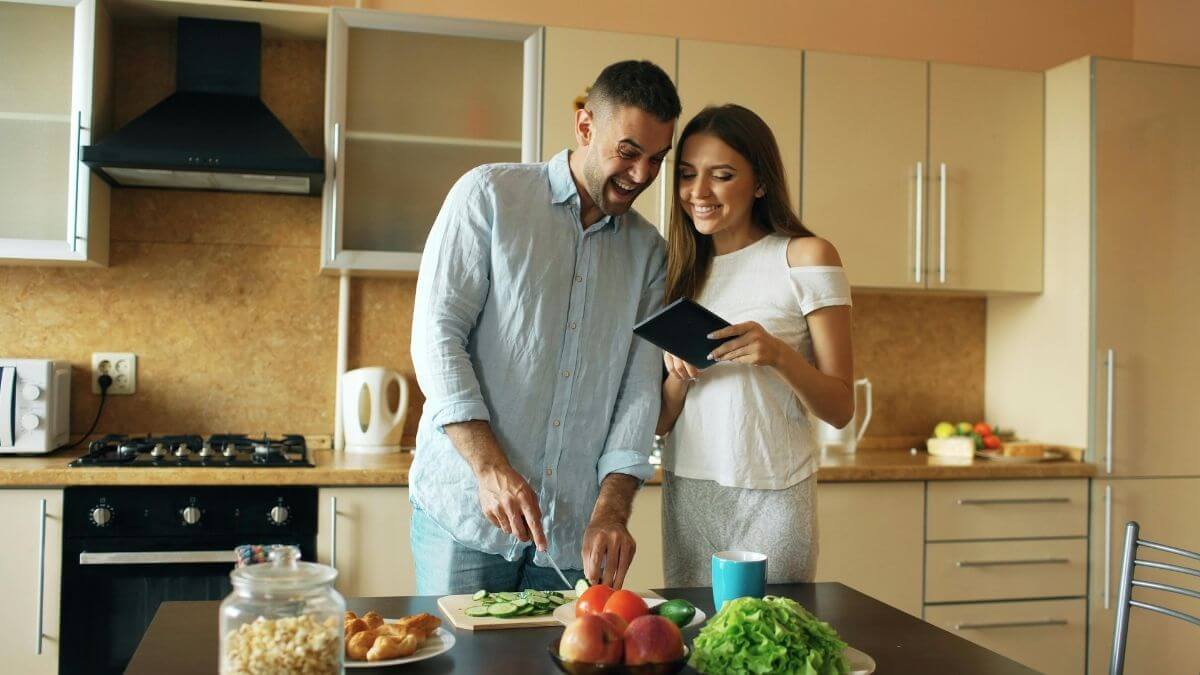 A couple laughing together while cooking and looking at a tablet in the kitchen