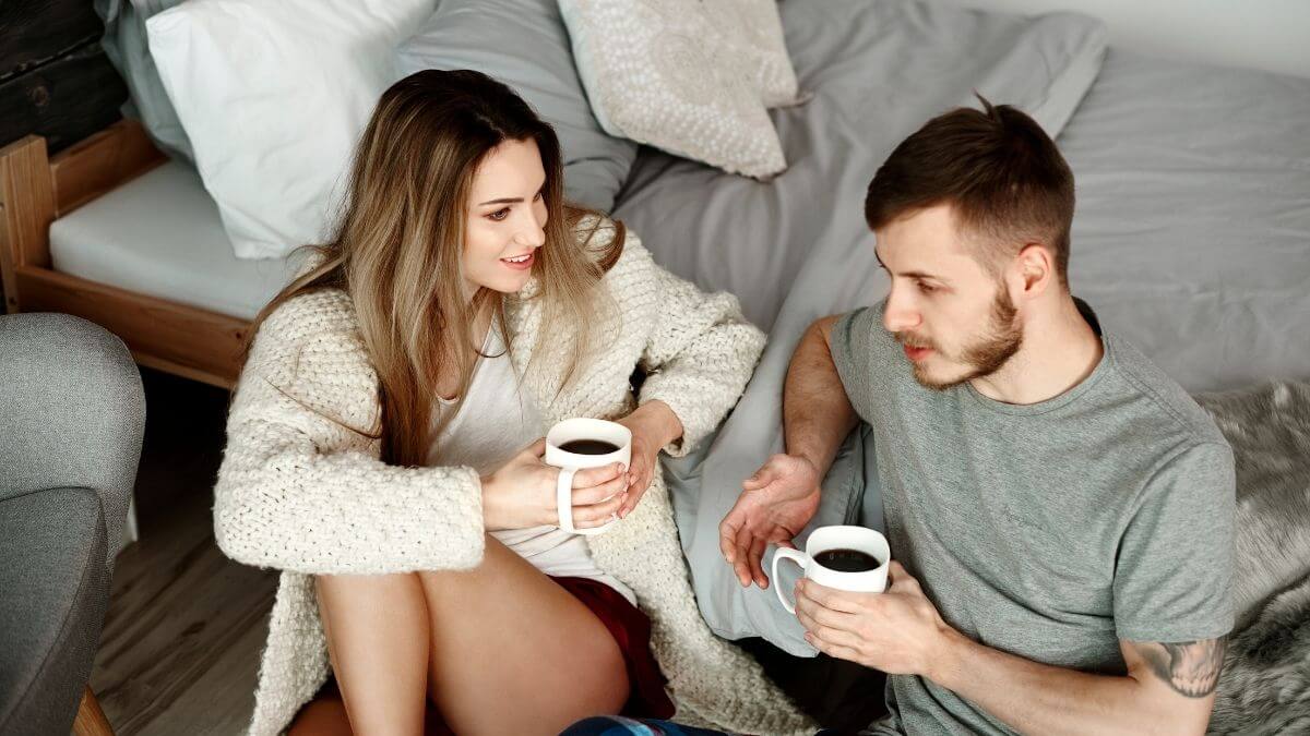 A couple sitting casually on the floor with coffee mugs, deep in conversation