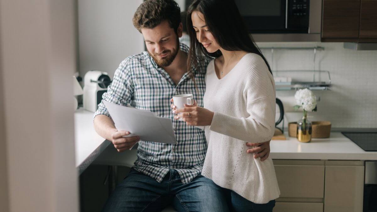 A couple standing together in the kitchen looking over a document