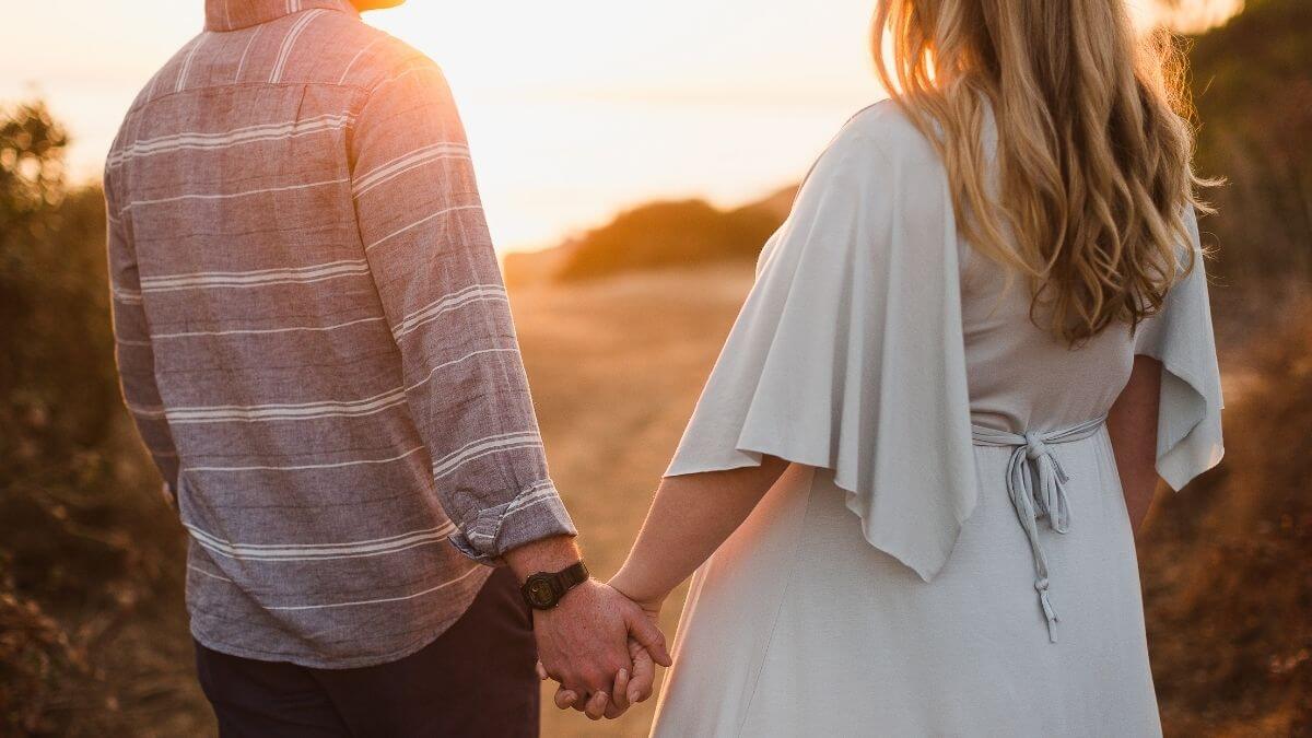 A couple holding hands and smiling at each other while walking through an autumn park