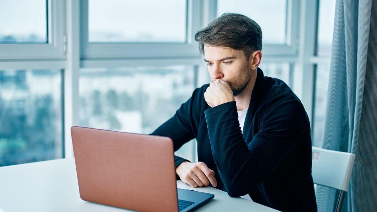 Man sitting at a desk looking thoughtfully at his laptop